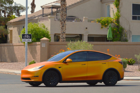 An orange colored, custom wrapped, Tesla Model Y electric car driving on a city street.